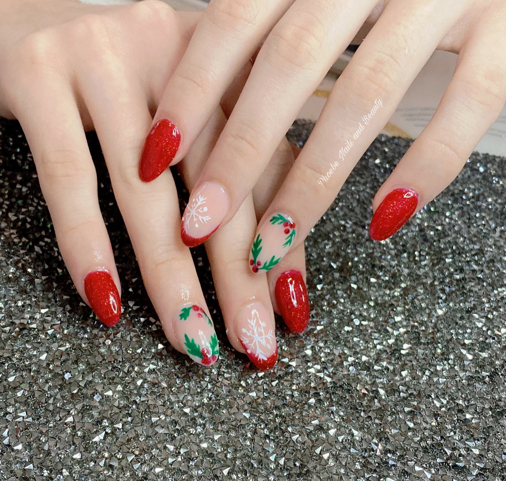 Red glitter almond nails with nude accent nails painted with white snowflakes and holly wreaths