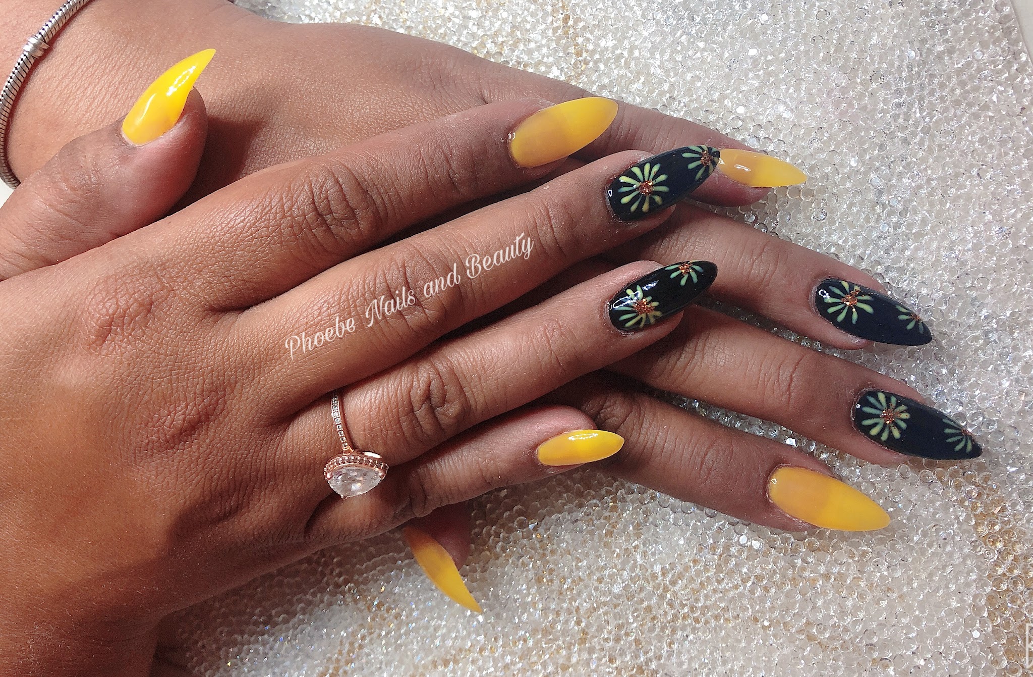 Long stiletto nails in yellow gel with black accent nails painted with green starbursts and gems